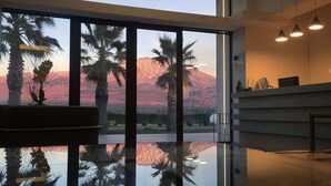Un interior moderno con ventanas amplias, suelo reflectante y vistas a palmeras y montañas.