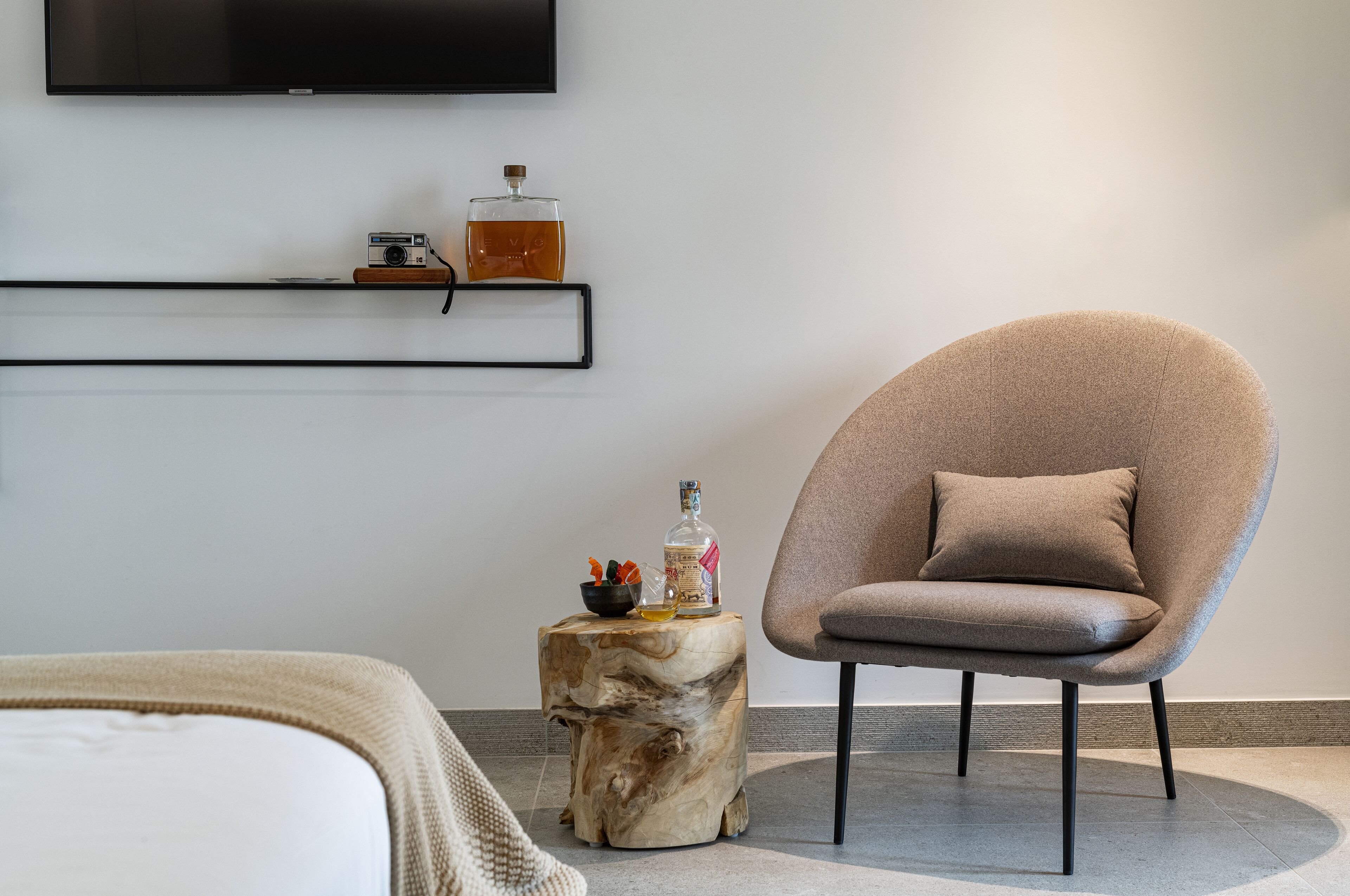 Quarto moderno com poltrona redonda, mesa lateral de madeira e televisão na parede.
