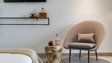 Quarto moderno com poltrona redonda, mesa lateral de madeira e televisão na parede.