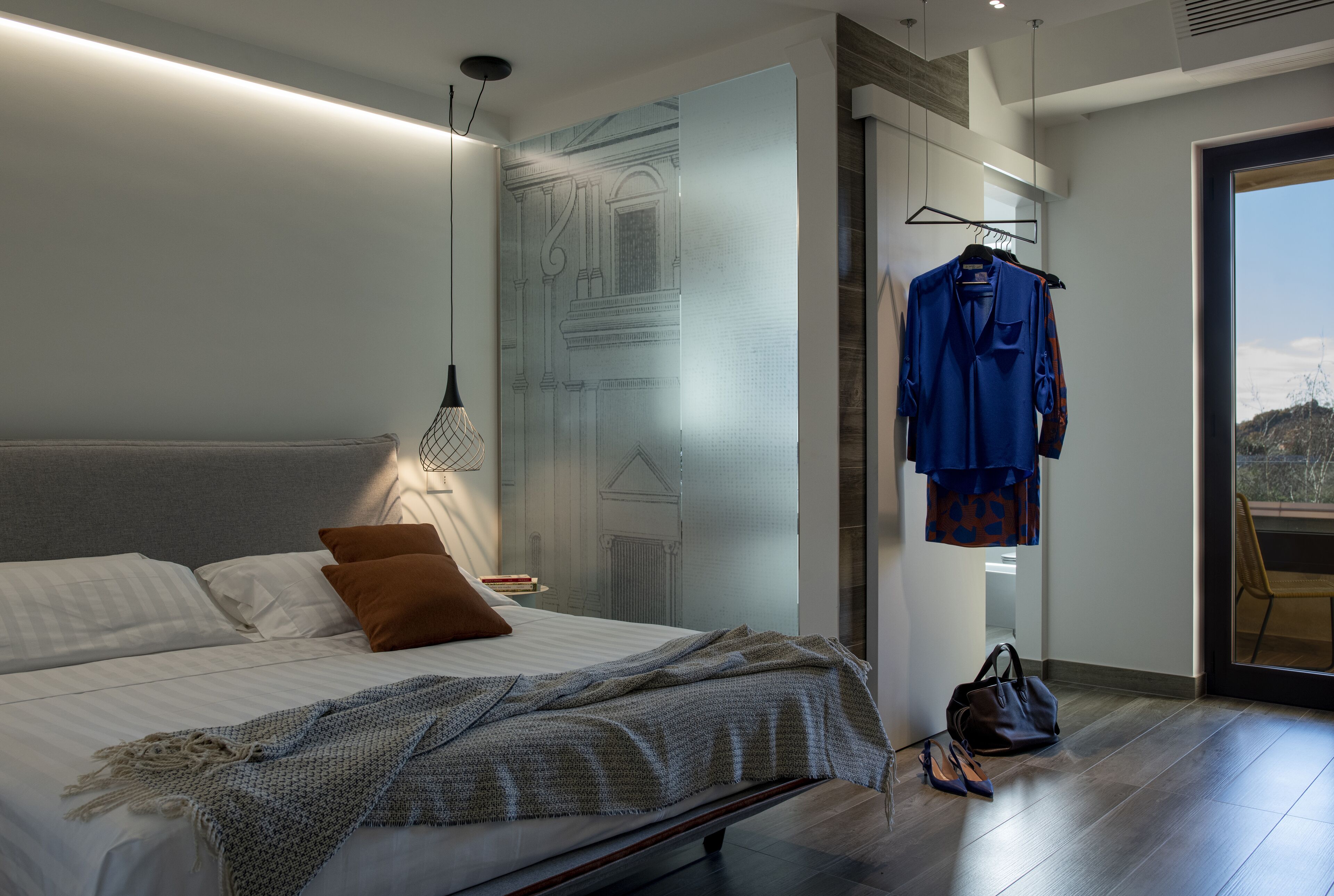 A modern bedroom with a large bed, a hanging garment rack, and a view of the outdoors.