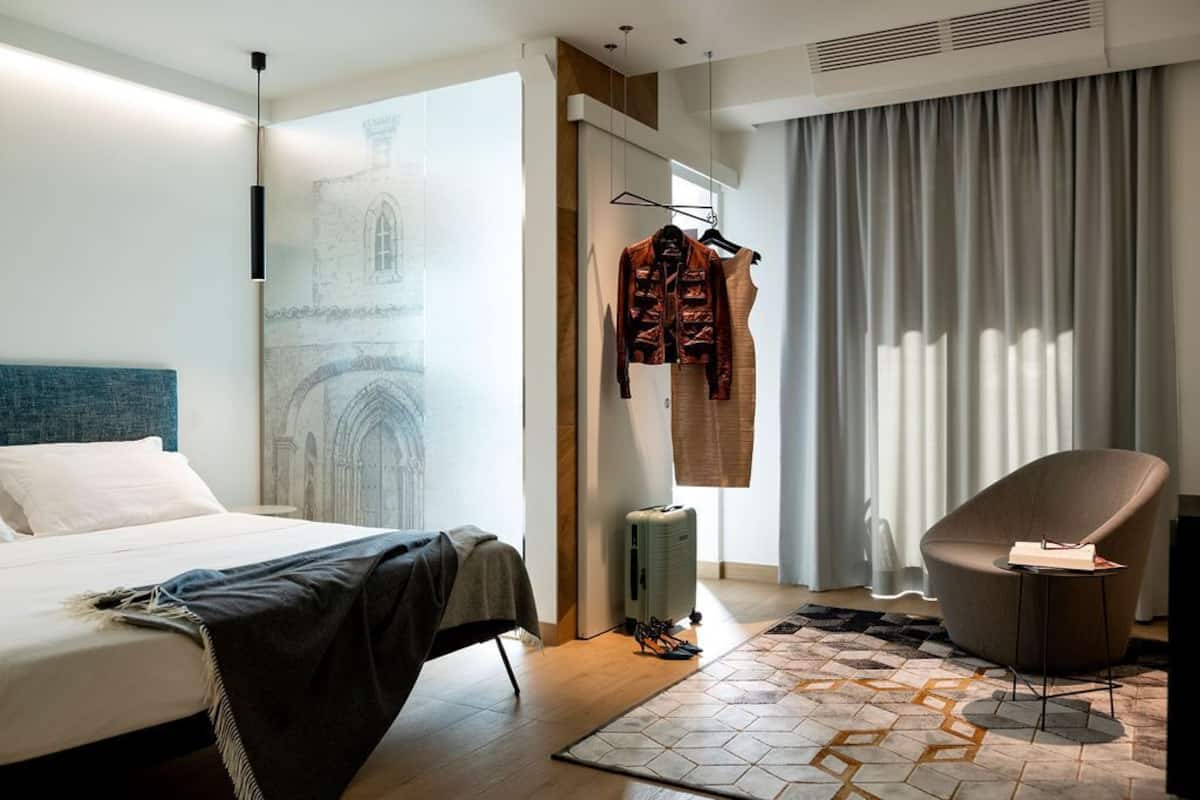 Una habitación de hotel moderna con una cama, una silla, una maleta y un perchero con ropa.