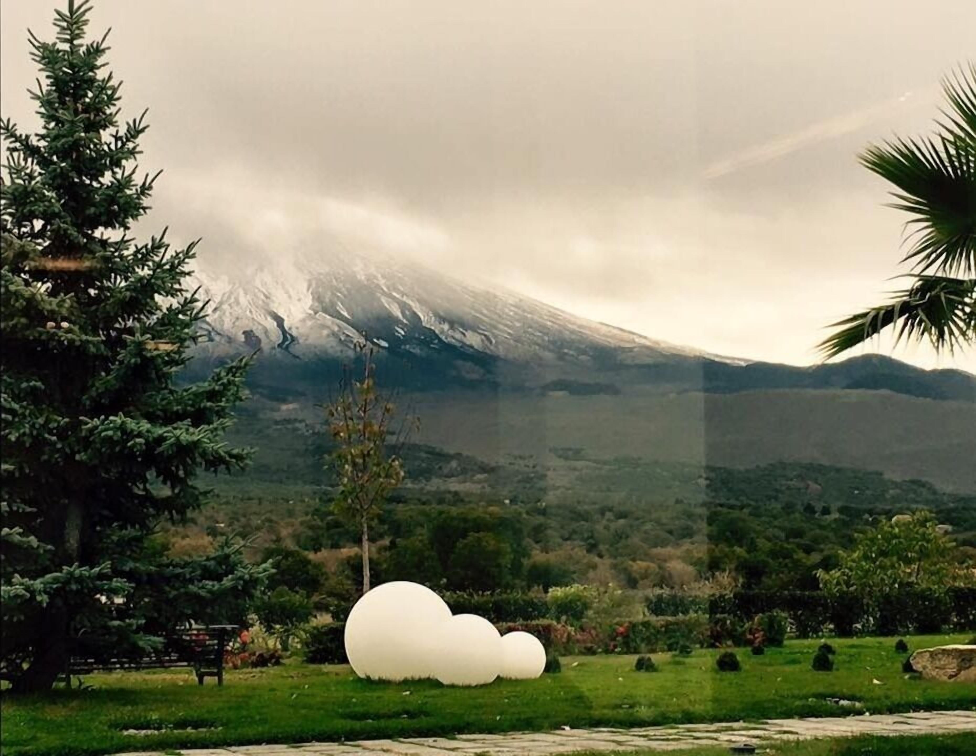 Un parc avec une grande sculpture représentant un nuage blanc, un banc et une montagne en arrière-plan.