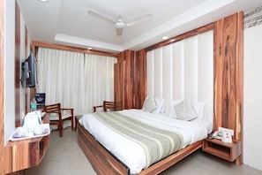 Une chambre d’hôtel avec un lit, des boiseries, une télévision, un bureau avec un plateau de petit-déjeuner et une fenêtre avec des rideaux.