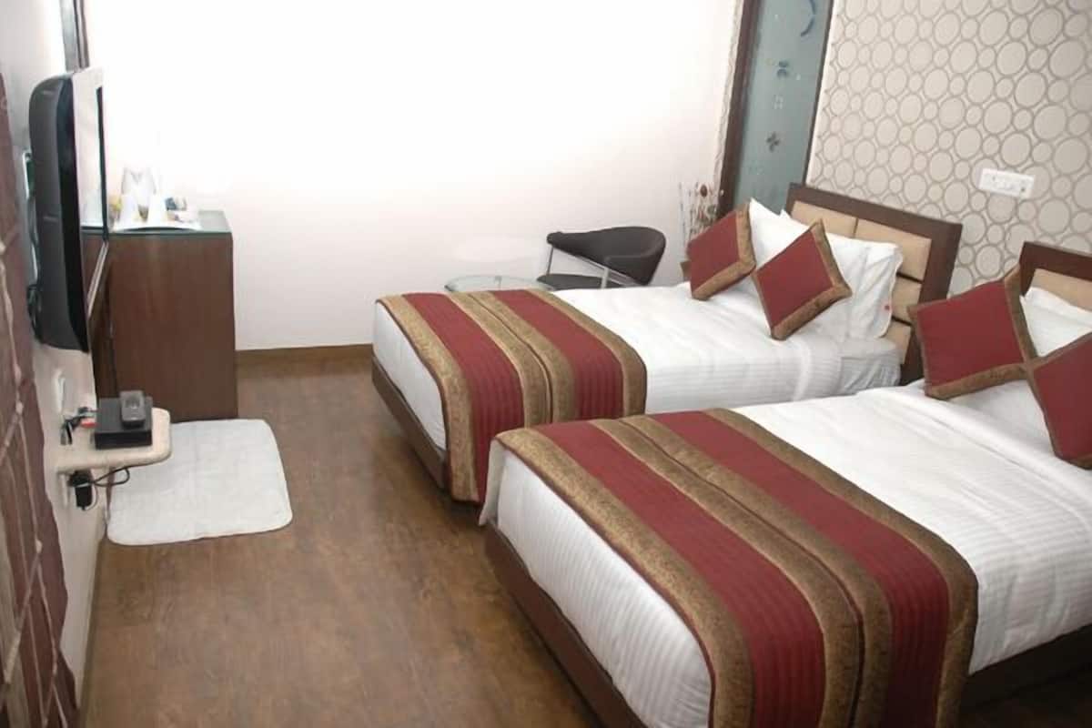 A hotel room with two beds, each with a red and white striped bedspread and matching pillows. There is a small desk with a chair and a flat-screen TV mounted on the wall.
