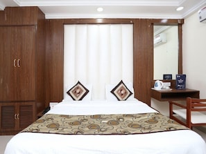 Une chambre d’hôtel comprenant un lit, une armoire en bois, une table de chevet avec une bouilloire et un miroir.