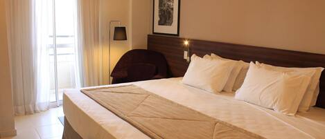 A hotel room with a large bed, a chair, a desk, and a window with curtains.