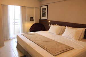 A hotel room with a large bed, a chair, a desk, and a window with curtains.