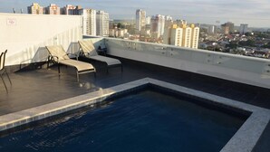 Una piscina en la azotea con sillones de descanso y vista a la ciudad.