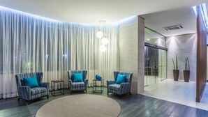 Un vestíbulo moderno con sillones a rayas, un tapete redondo y un muro de cristal que da a un pasillo.