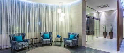 Un vestíbulo moderno con sillones a rayas, un tapete redondo y un muro de cristal que da a un pasillo.