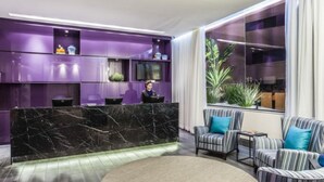 Una zona de recepción con mostrador de mármol, estanterías moradas y sillones a rayas.