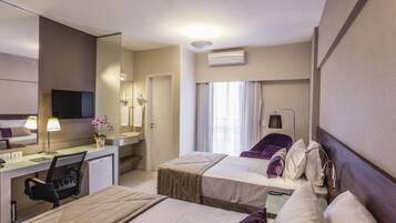 A hotel room with two beds, a desk, a chair, a TV, and an air conditioning unit.