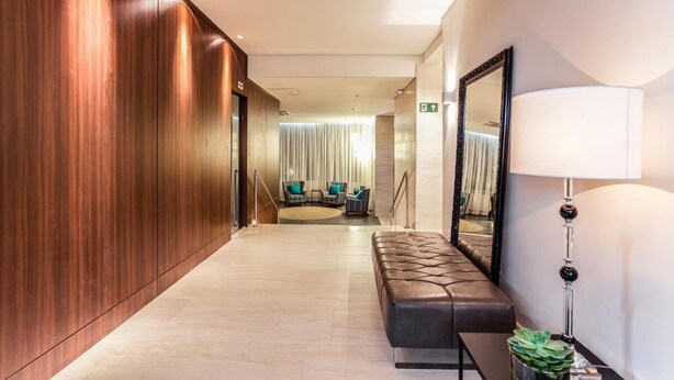 Un moderno vestíbulo de hotel con una pared de madera, una zona de estar con sofá y sillones, y un espejo grande.