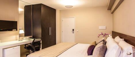 A hotel room with a bed, a desk with a chair, a television, and a door.