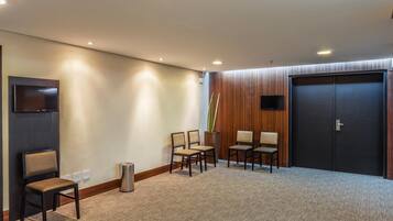 A hotel lobby with a carpeted floor, a reception desk, a flat-screen TV, and a large wooden door.