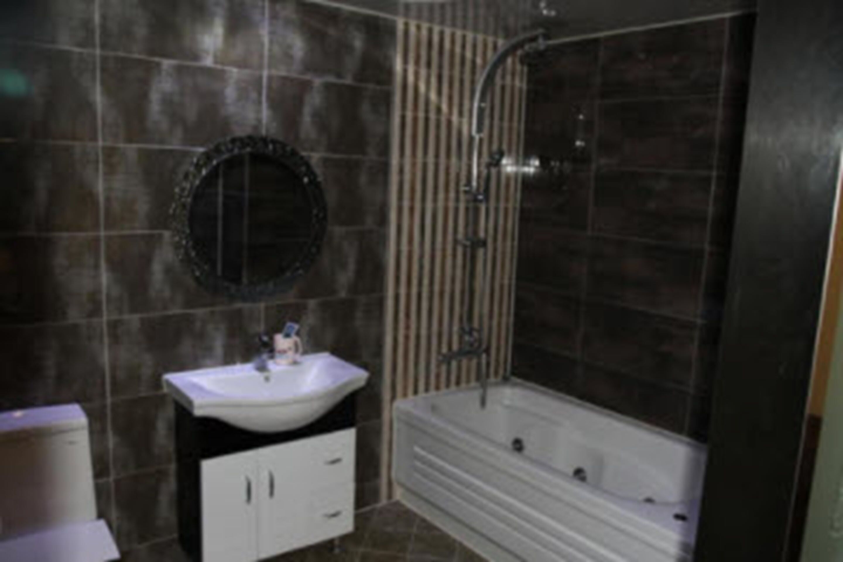 Un baño con un lavamanos blanco, un espejo redondo y una bañera.