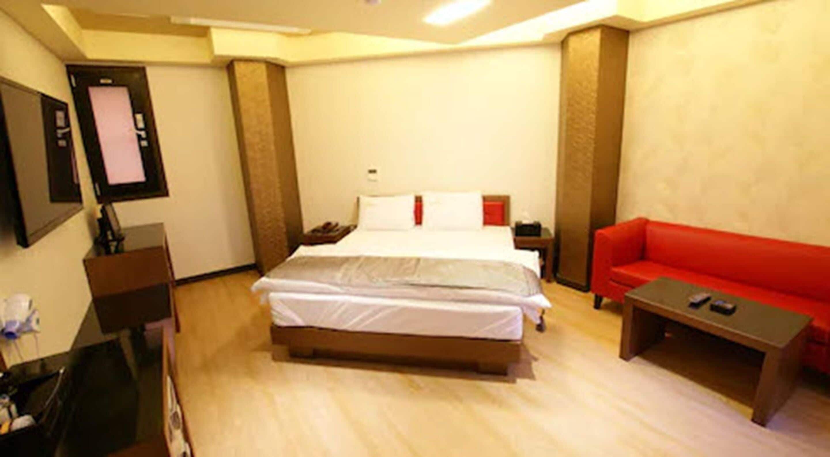 Une chambre d’hôtel avec un lit, un canapé rouge, une petite table et un bureau avec un ordinateur.
