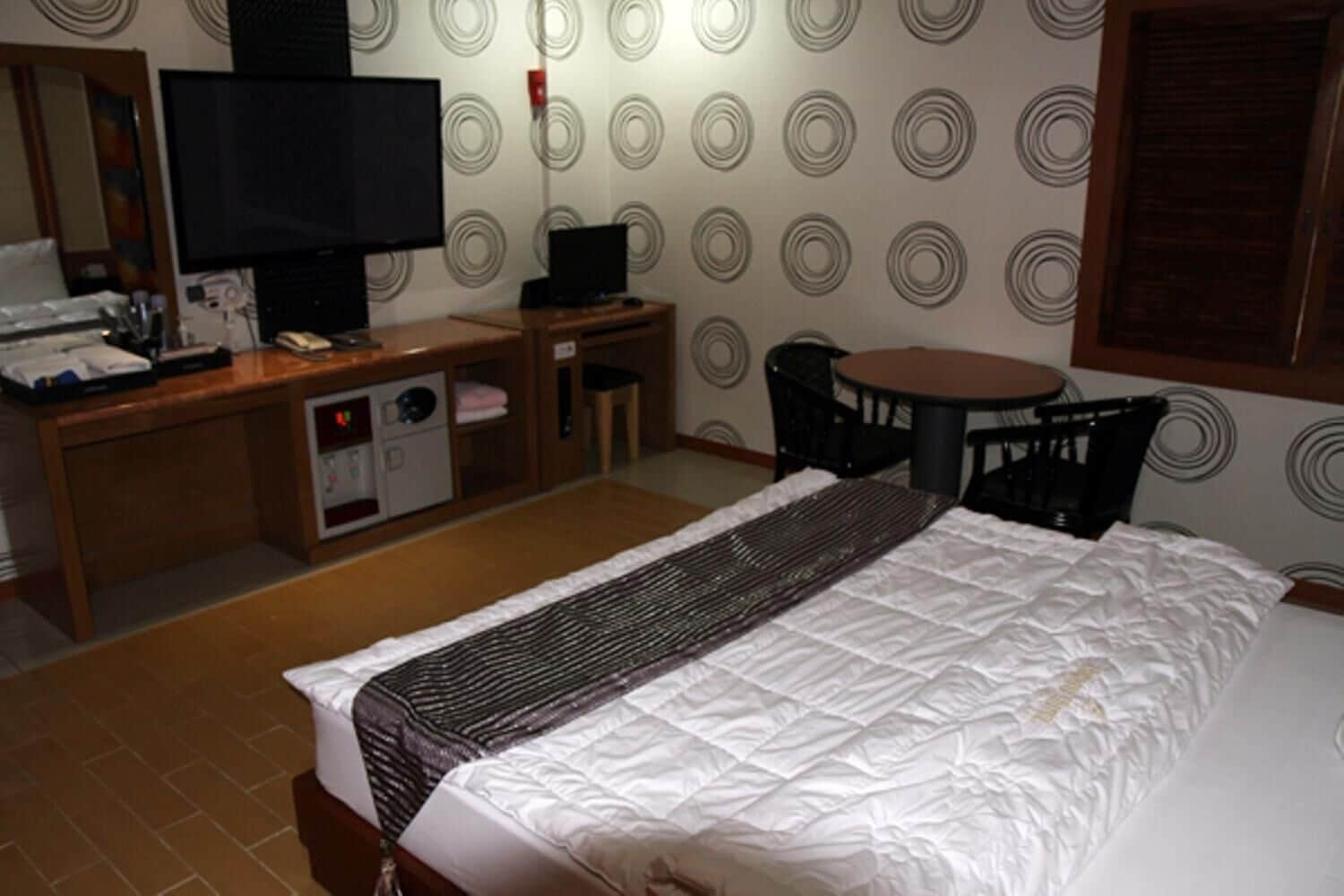 A hotel room with a bed, a desk with a computer, a TV, and a small table with chairs.