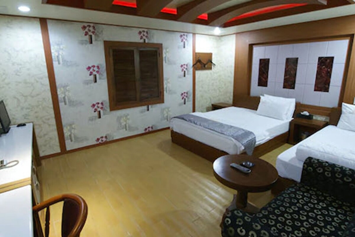 A hotel room with two beds, a desk, a chair, and a small table.