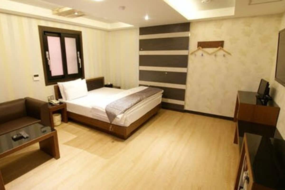 A hotel room with a bed, a desk, a chair, a TV, and a wardrobe.