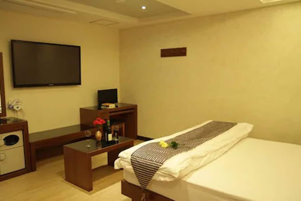 A hotel room with a bed, a TV, a desk, and a small table with a vase.