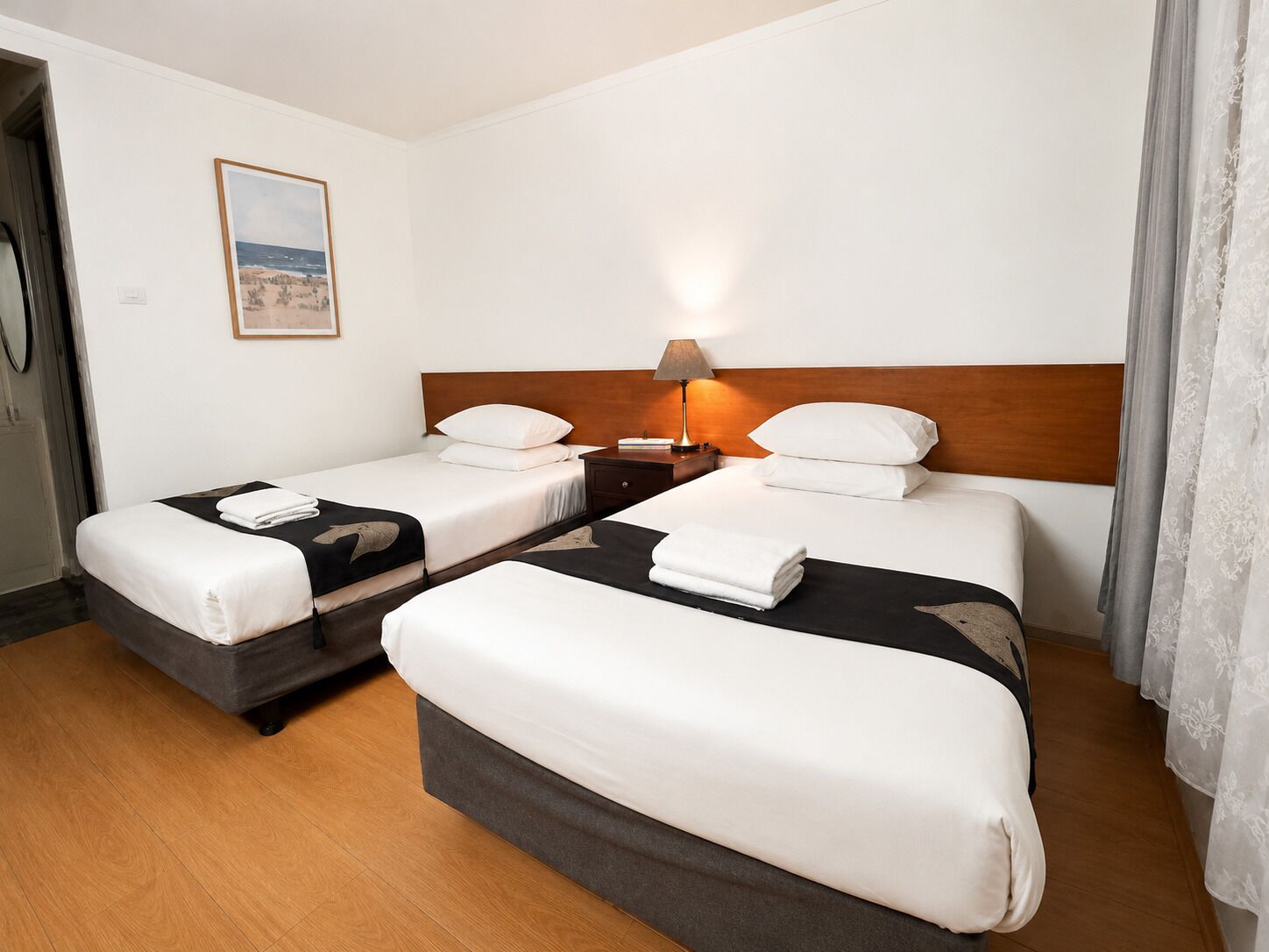 Een hotelkamer met twee bedden, een nachtkastje, een lamp en een schilderij aan de muur.