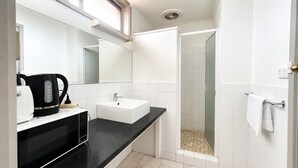 A modern bathroom with a black countertop, white sink, and a glass-enclosed shower. - Beaconsfield Lodge Motel (Beaconsfield)