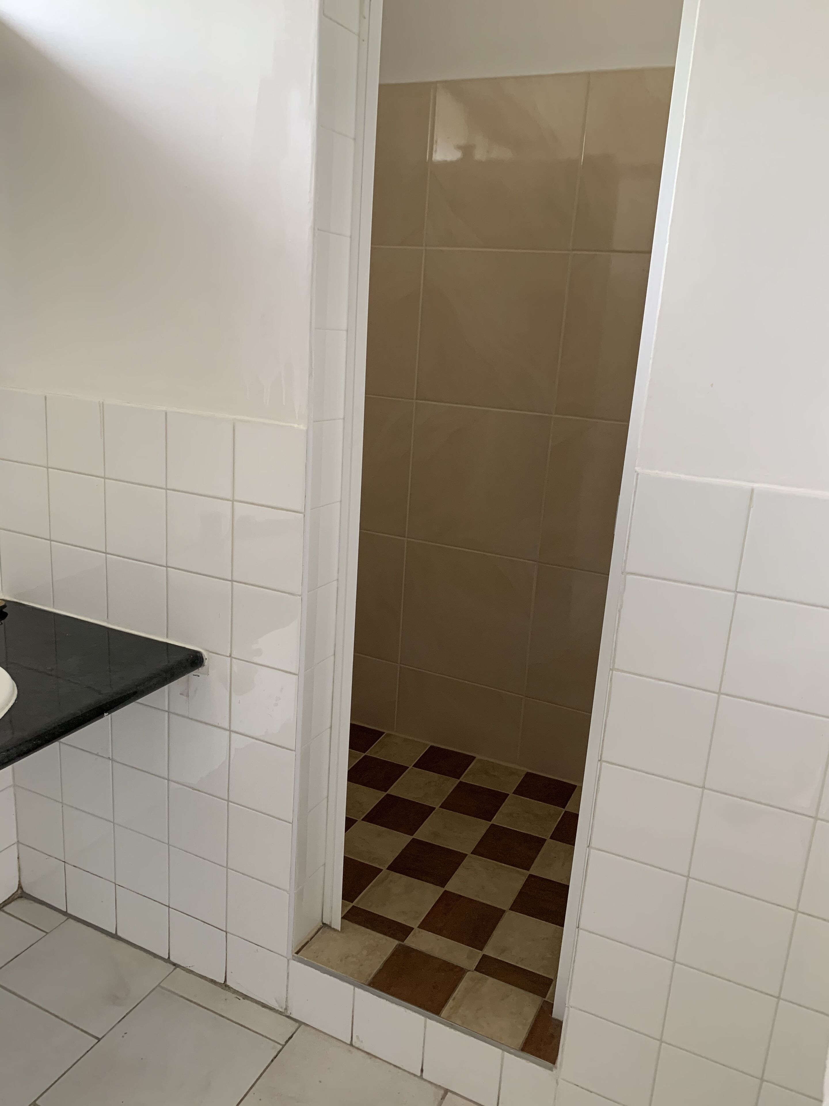 A bathroom with white tiled walls, a black countertop, and a shower area with beige and brown checkered tiles.