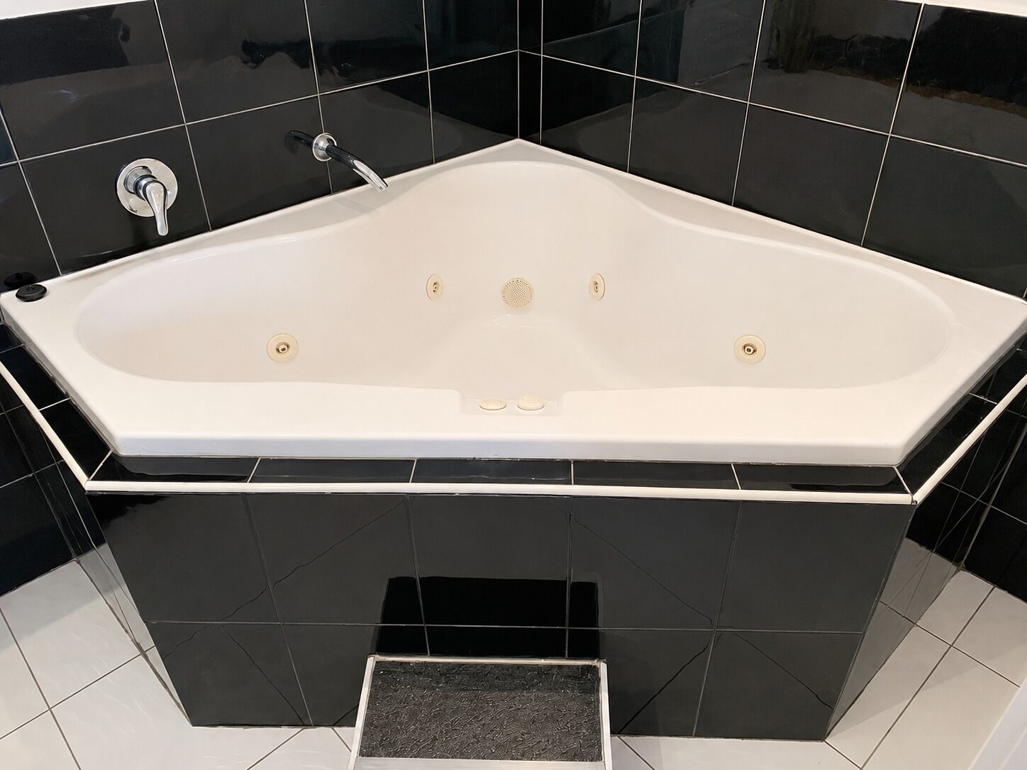 Un bagno moderno con una vasca freestanding, pareti rivestite di piastrelle nere e pavimento bianco.