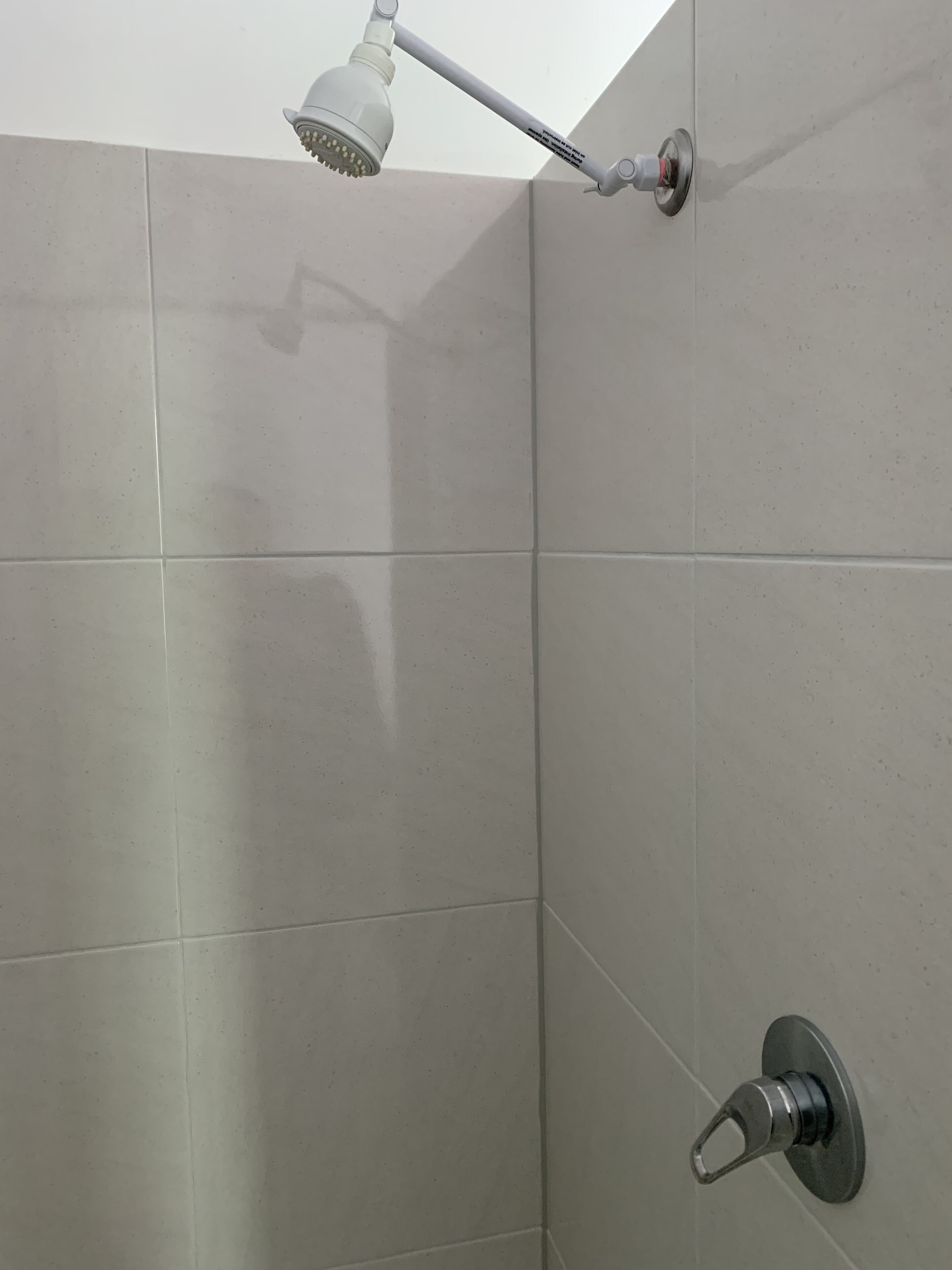 A shower with a handheld showerhead mounted on a wall, a wall-mounted control knob, and a corner tile design.