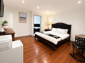 A hotel room with a bed, a desk, a chair, a lamp, and a view of the sea. - Beaconsfield Lodge Motel (Beaconsfield)