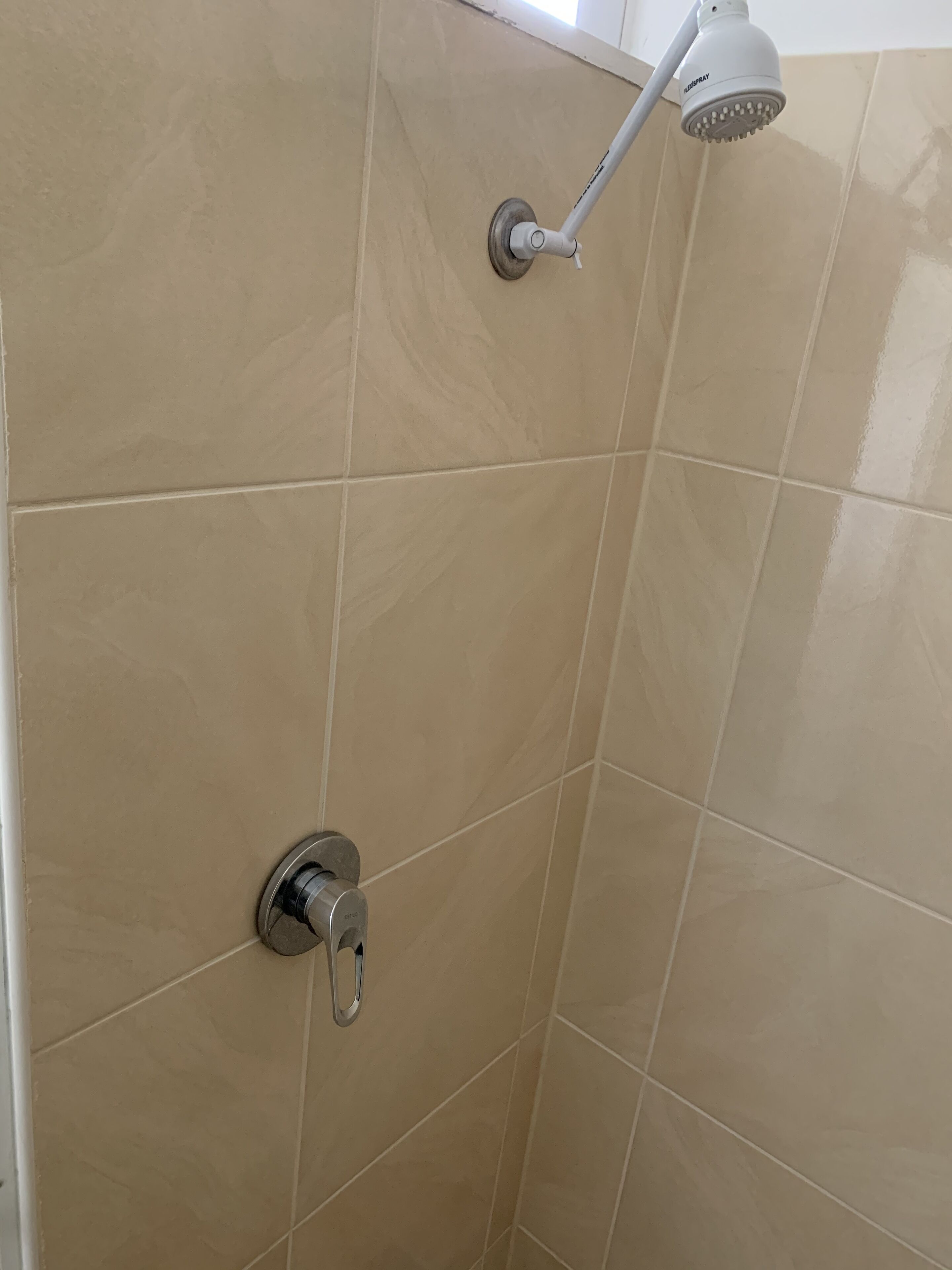 A bathroom with beige tiles, a showerhead, and a faucet.