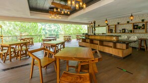 A spacious restaurant with wooden tables and chairs, a bar area, and large windows offering a view of greenery. - Driam Riverside Resort (Pasirjambu)