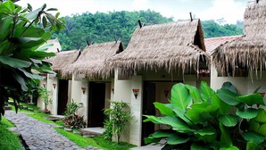 A row of thatched-roof huts with a stone pathway leading to them, surrounded by lush greenery. - Driam Riverside Resort (Pasirjambu)