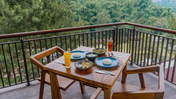 A wooden table with a meal set on a balcony overlooking a forested area. - Driam Riverside Resort (Pasirjambu)