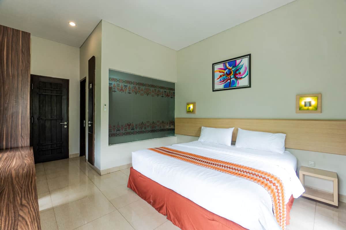 A hotel room with a large bed, a wooden headboard, a decorative wall panel, and a framed artwork.