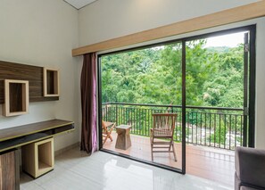 Quarto moderno com varanda, escrivaninha de madeira e vista para vegetação exuberante.