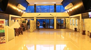 Eine geräumige Lobby mit hoher Decke, großen Fenstern und einem offenen zentralen Bereich mit einer Glastür zu einer Außen-Sitzgelegenheit.