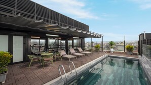 A rooftop pool area with lounge chairs and a table, surrounded by a modern building with large windows. - SQ HANG GAI HOTEL & SPA (Hanoi)