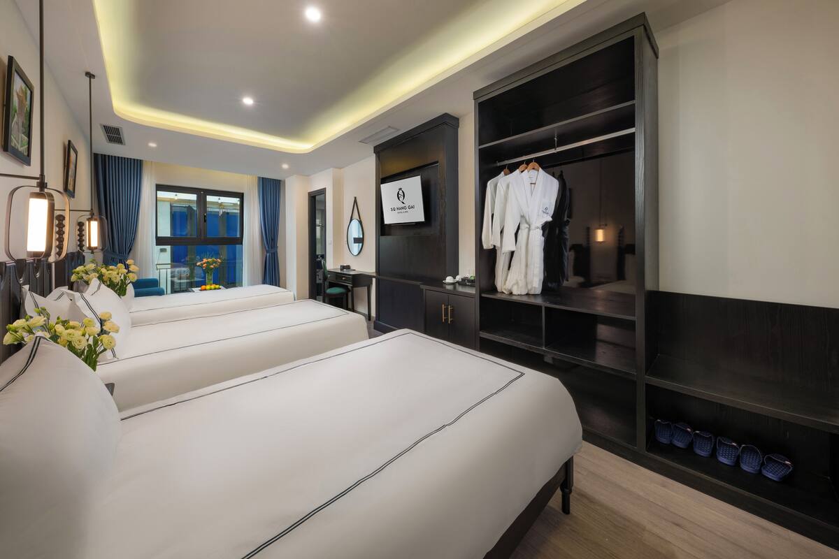 A hotel room with two beds, a wardrobe, a vanity, and a large window with curtains.