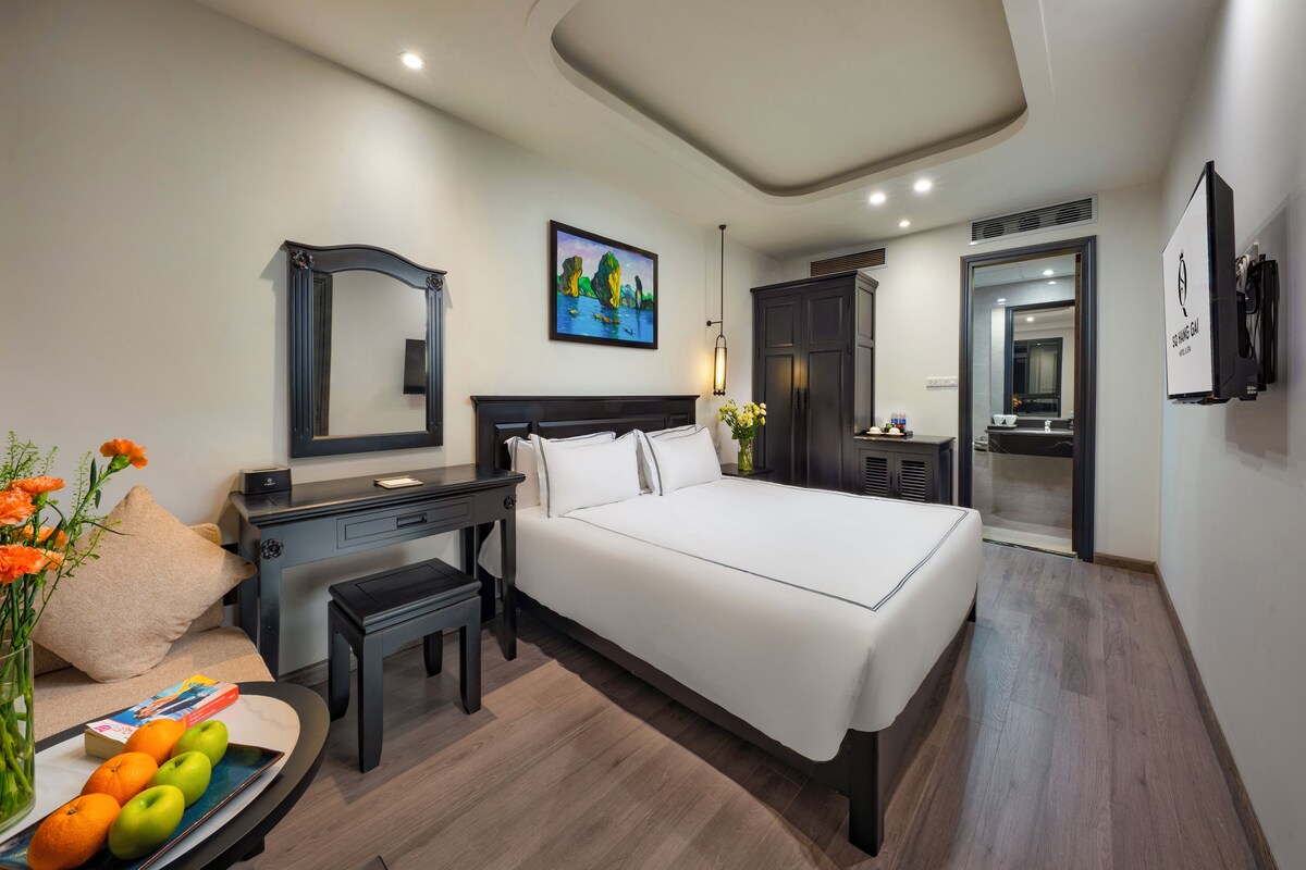 A hotel room with a large bed, a desk with a chair, a vanity with a mirror, and a bathroom with a shower and sink.