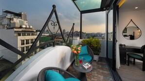 A modern balcony with a glass ceiling, wicker furniture, a small table with drinks, and a view of the cityscape. - SQ HANG GAI HOTEL & SPA (Hanoi)