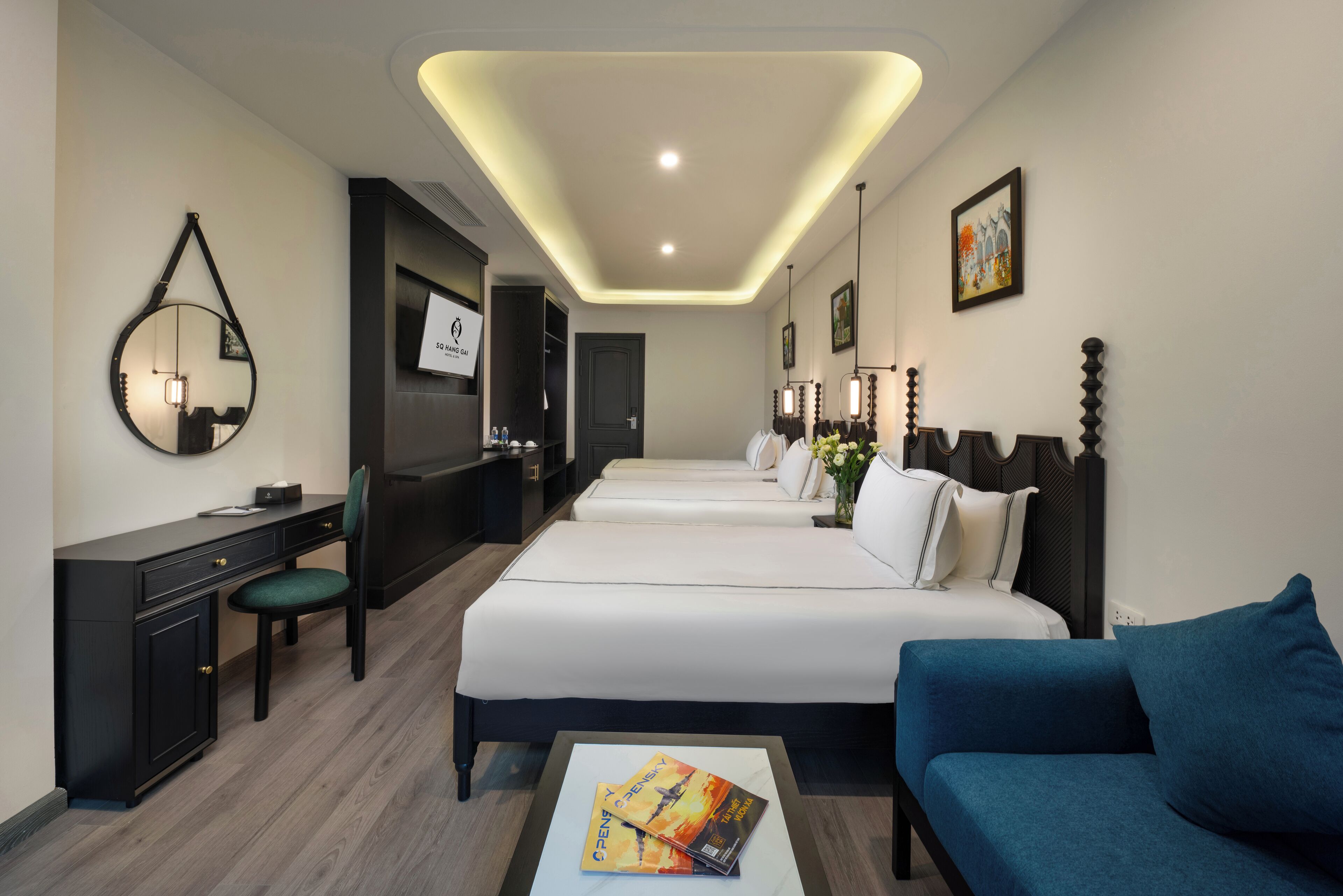 A hotel room with a desk, two beds, a sofa, and a mirror.