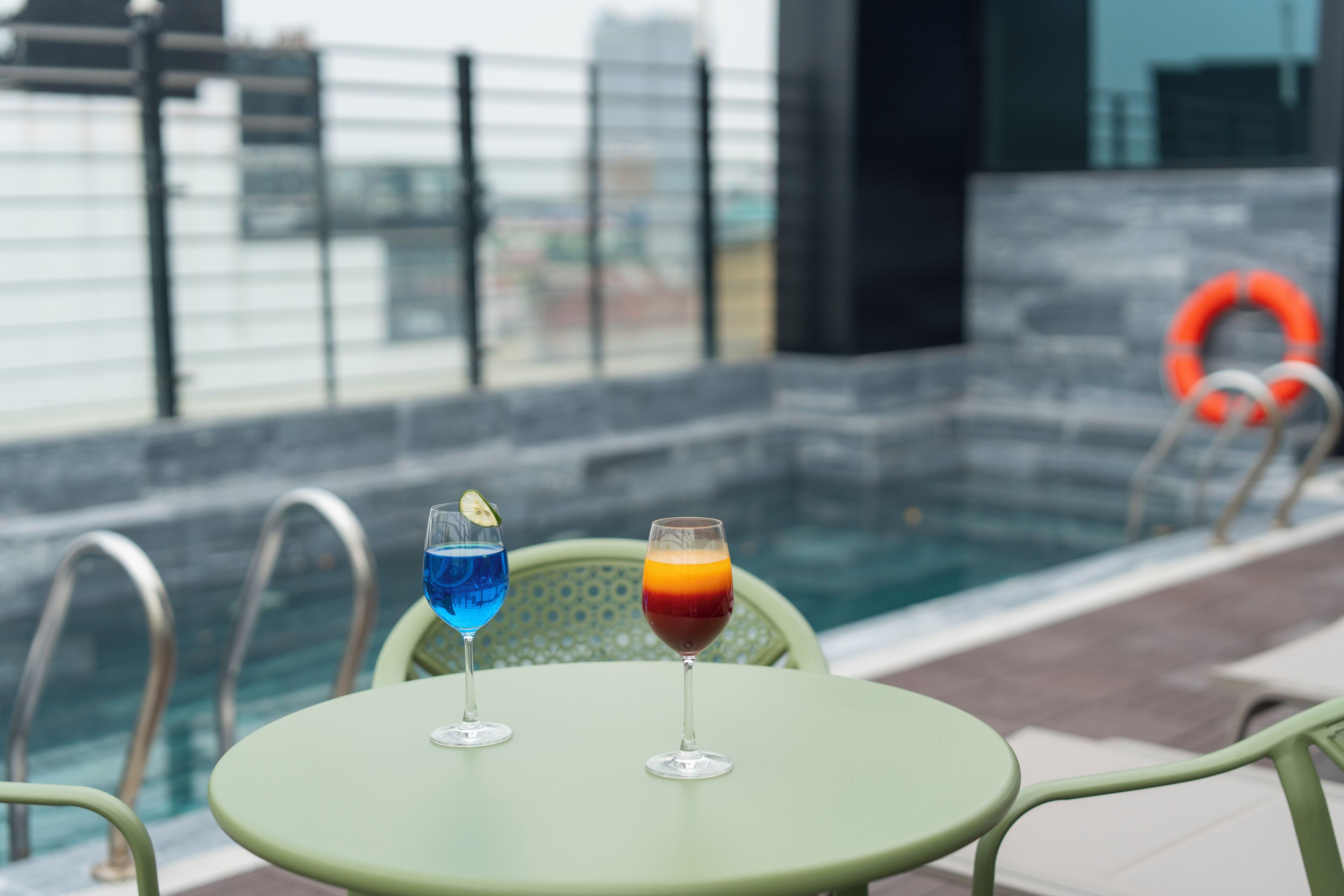Deux cocktails sur une table verte, près d’une piscine, avec une bouée de sauvetage visible en arrière-plan.