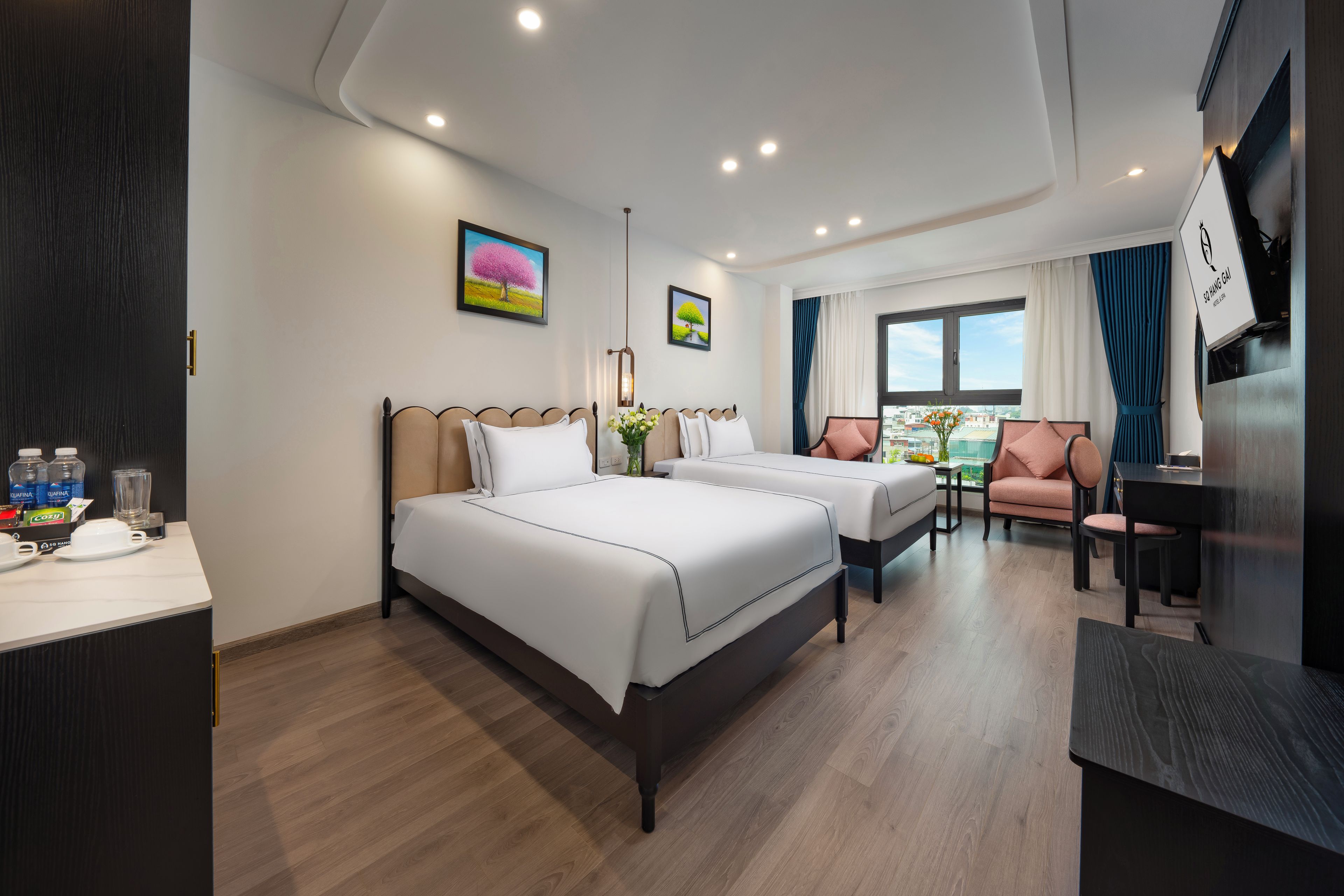 Une chambre d’hôtel avec deux lits, un bureau, une chaise, une télévision et une fenêtre donnant sur la ville.
