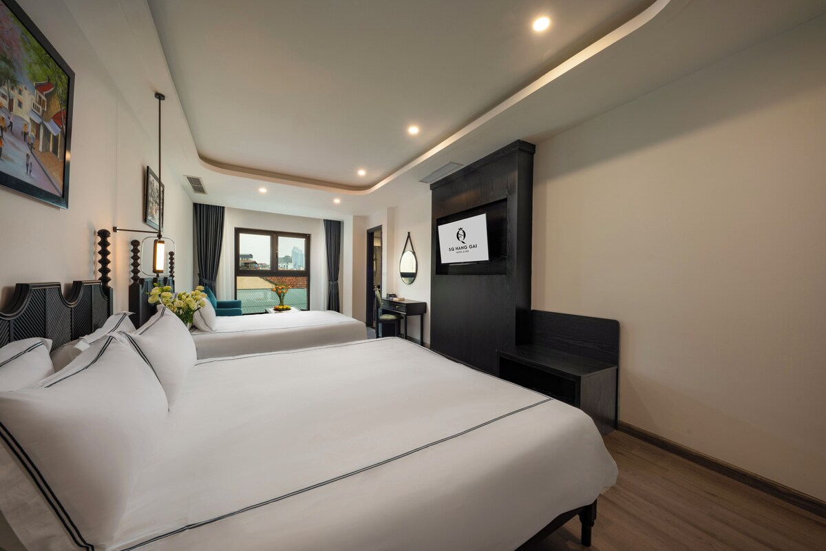 A hotel room with two beds, a desk, a chair, a TV, and a painting on the wall.