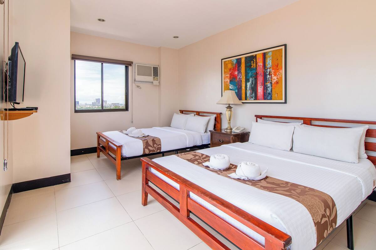 A hotel room with two beds, a TV, an air conditioning unit, and a window with a city view.