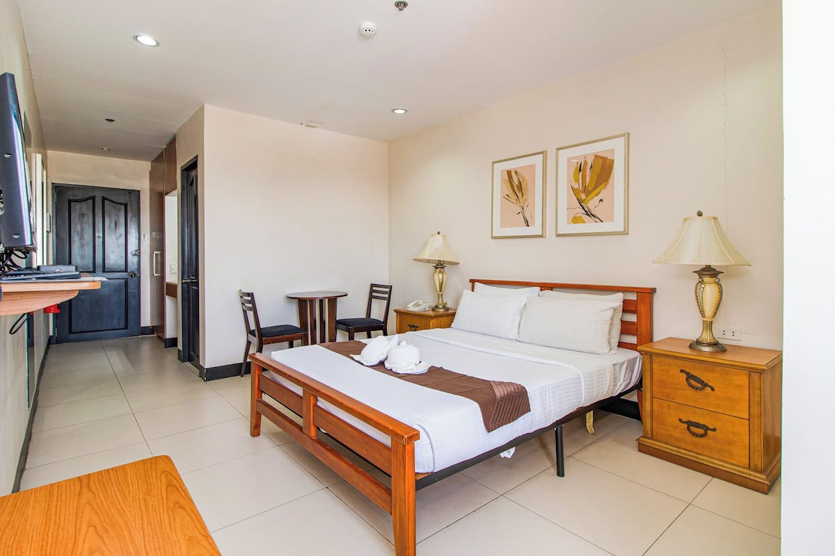 A hotel room with a bed, bedside tables, a desk, chairs, and artwork on the walls.