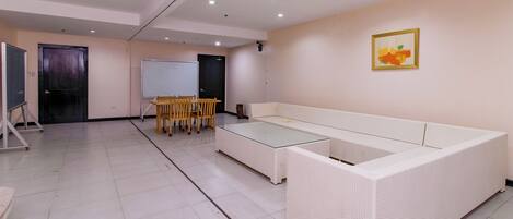 A room with a white sofa, a glass-top table, and a whiteboard.