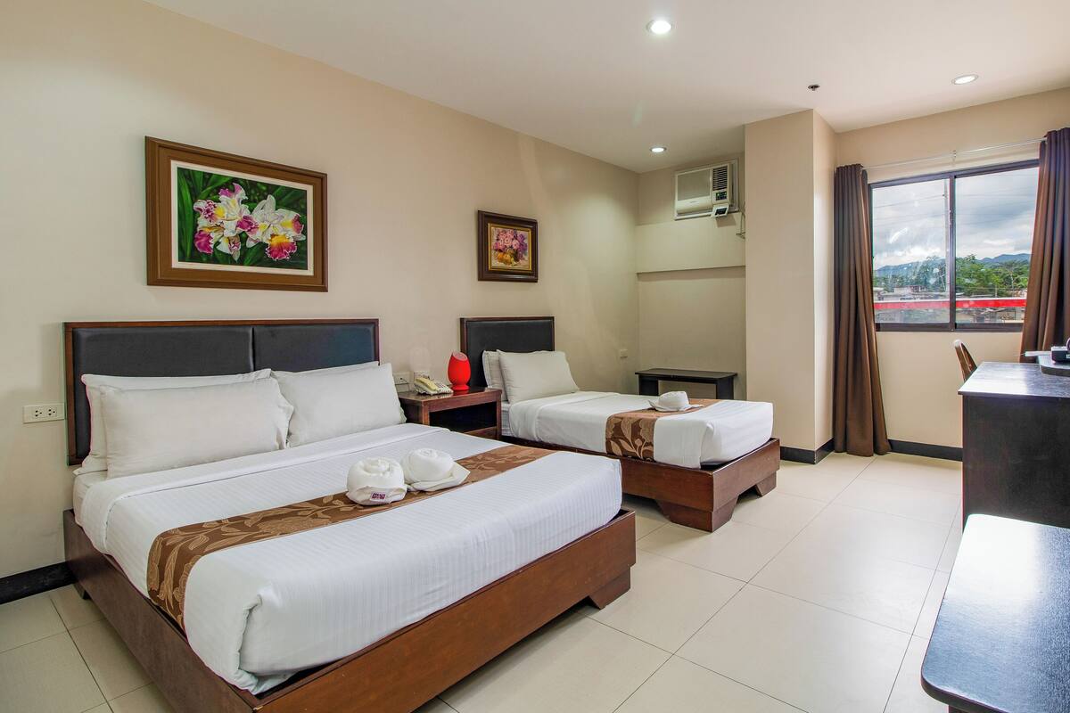 A hotel room with two beds, a desk, a chair, and a window with curtains.